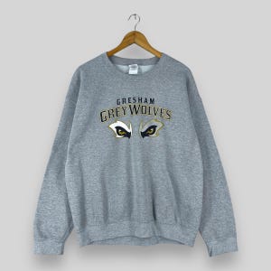 Può includere: Felpa grigia con il testo "GRESHAM GREY WOLVES" e una grafica di occhi di lupo in oro e nero.