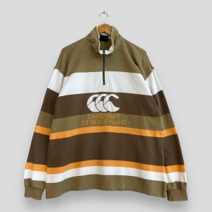 May include: A brown, white, and orange striped rugby shirt with a Canterbury of New Zealand logo.