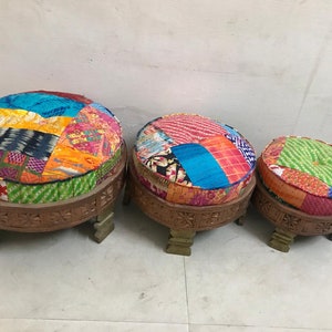 May include: Three round, colorful, patchwork fabric covered ottomans with wooden legs. The ottomans are arranged in size order from largest to smallest.