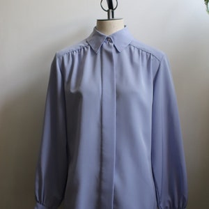 以下が含まれることがあります： 襟付きのライトブルーの長袖ボタンダウンシャツ。シャツはマネキンに着せられており、ゆったりとしたフィット感です。