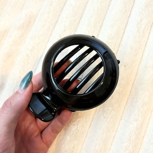Peut inclure: Pince à cheveux en plastique noir avec un design rond et ouvert. La pince a cinq dents pour maintenir les cheveux.