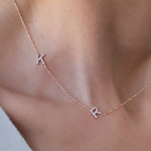 Könnte beinhalten: Eine zarte goldene Kettenkette mit zwei kleinen, mit Diamanten besetzten Buchstaben "K" und "R", die daran hängen.