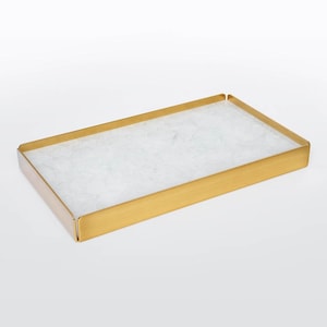 May include: Rectangular decorative tray with a gold-coloured metal frame and a white, textured interior. The tray has a minimalist design and is suitable for various home decor uses.
