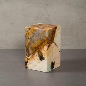 Può includere: Un blocco di pietra rettangolare con un motivo naturale multicolore. I colori includono sfumature di marrone, oro e crema, con aree più scure e venature. Il blocco ha un aspetto lucido e una forma geometrica solida.