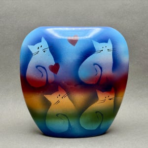 May include: A blue vase with a gradient of colours, featuring white cat silhouettes with black whiskers and red hearts. The vase has a rounded shape and a smooth surface, ideal for home decor.