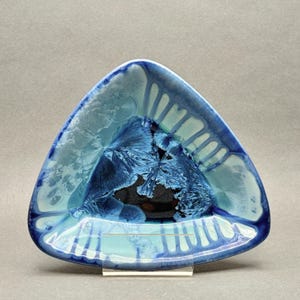 May include: A triangular ceramic dish featuring a crystalline glaze with deep navy blue and light turquoise hues. The surface displays intricate, star-like crystal formations radiating from the centre, with dark blue drips along the edges.