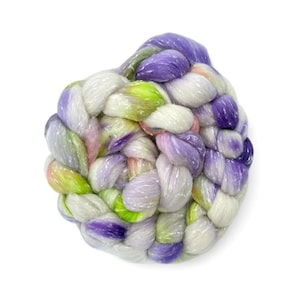 May include: A thick, braided hank of roving fibre featuring a variegated colour palette of white, bright lime green, soft lavender, and deep purple. The texture is fluffy and soft, with the individual strands twisted together into a dense coil.