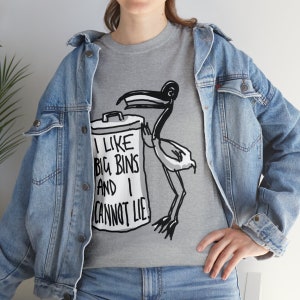 May include: A gray t-shirt with a black and white illustration of a bird holding a trash can. The text on the trash can reads "I like big bins and I cannot lie."