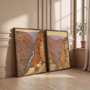 May include: Two framed rectangular wall art prints depicting a canyon landscape with steep orange and brown rock formations, a winding river at the base, and a pale yellow sky. The artwork features detailed textures and earthy tones in a vertical orientation.