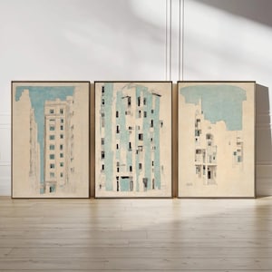 May include: A set of three framed wall art prints featuring architectural sketches of buildings. Each print displays a cream-colored background with light blue accents, depicting multi-story structures with windows and balconies in a vertical orientation.