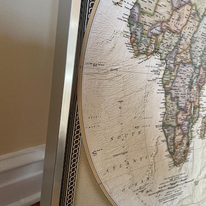 a detailed map of the world, with various countries and regions clearly marked. The map is framed and displayed on a wall, providing a comprehensive view of the world's geography.