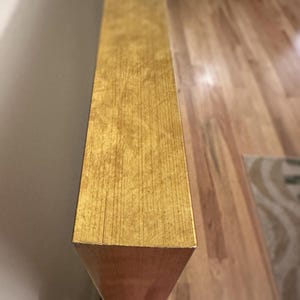a close-up view of a wooden surface with a textured, golden-colored finish, likely a piece of furniture or a decorative element.