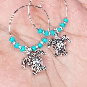 Peut inclure: Boucles d'oreilles créoles argentées avec des perles turquoise et un pendentif en forme de tortue argentée.