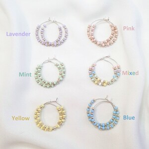 May include: Six pairs of hoop earrings with silver hoops and colorful beads. The colors are lavender, pink, mint, mixed, yellow, and blue.