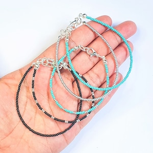 May include: Three beaded bracelets in black, silver and turquoise. The bracelets are layered on a hand.