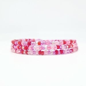 May include: A multi-strand bracelet made of pink and red seed beads. The bracelet is made of several strands of beads that are woven together.