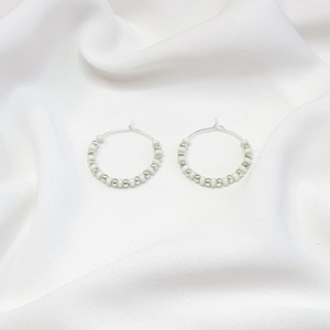 May include: A pair of silver hoop earrings with light green beads.