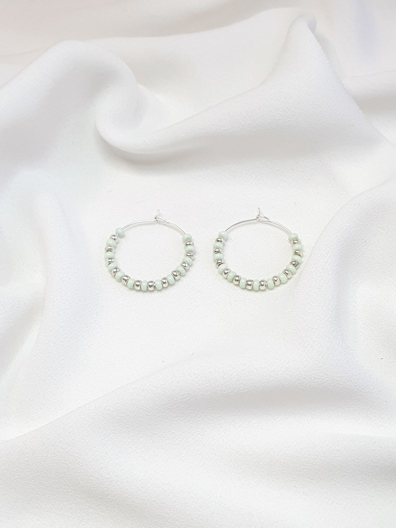 May include: A pair of silver hoop earrings with light green beads.