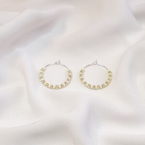 May include: A pair of silver hoop earrings with small, cream-colored beads.