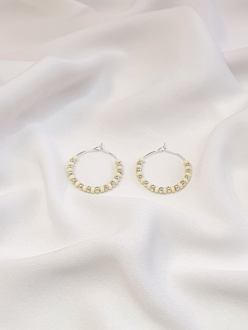 May include: A pair of silver hoop earrings with small, cream-colored beads.