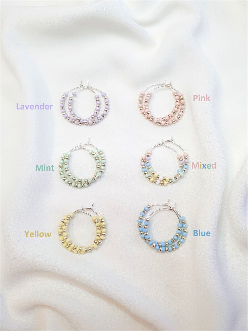 May include: Six pairs of hoop earrings with silver hoops and colorful beads. The colors are lavender, pink, mint, mixed, yellow, and blue.