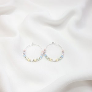 May include: A pair of silver hoop earrings with pastel colored beads. The beads are arranged in a gradient pattern, starting with pink and transitioning to light blue.