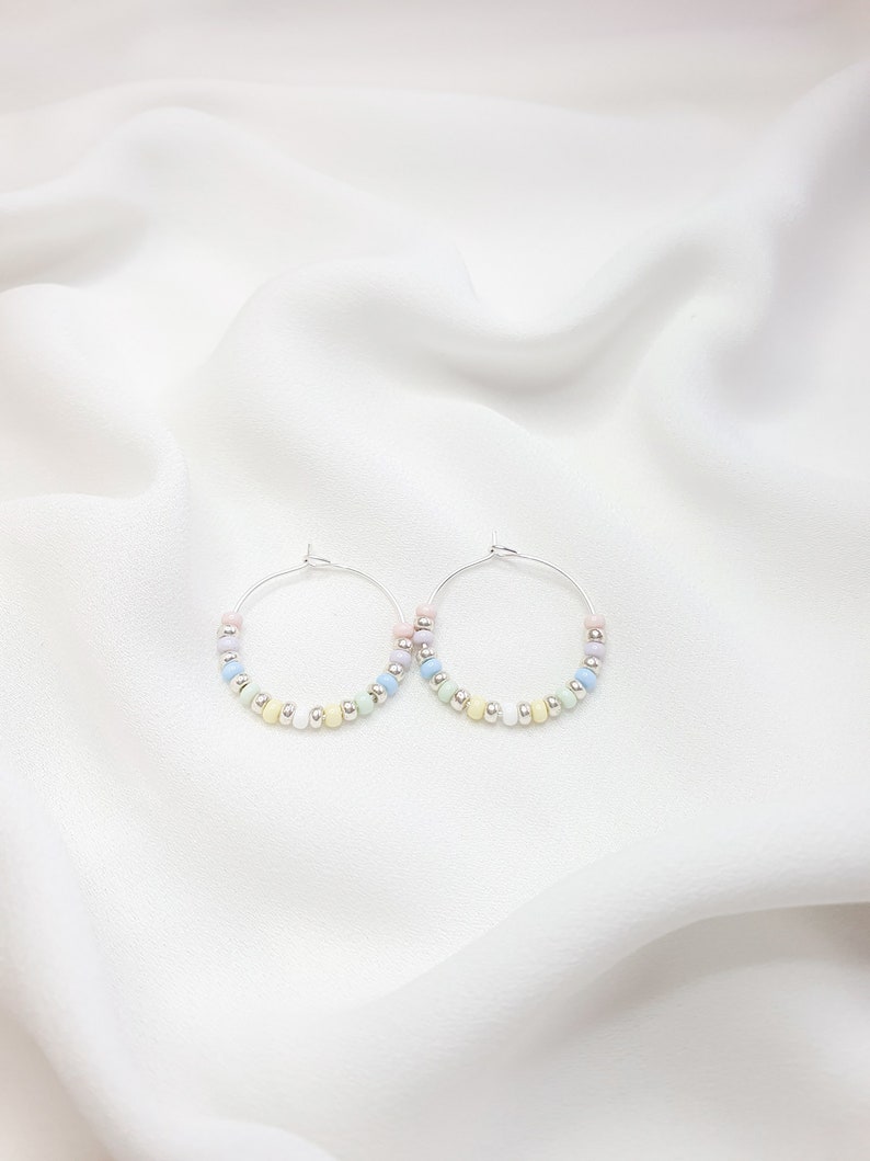 May include: A pair of silver hoop earrings with pastel colored beads. The beads are arranged in a gradient pattern, starting with pink and transitioning to light blue.