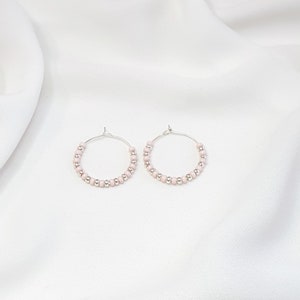May include: A pair of silver hoop earrings with small pink beads.