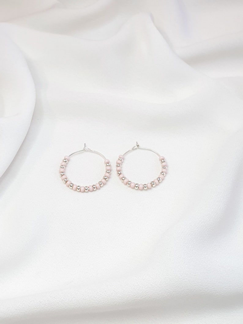 May include: A pair of silver hoop earrings with small pink beads.