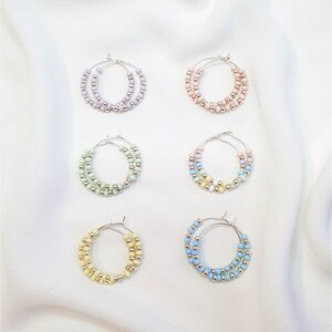 May include: Six pairs of hoop earrings with pastel colored beads. The earrings are arranged in two rows of three. The colors are lavender, pink, light green, light blue, yellow, and blue.