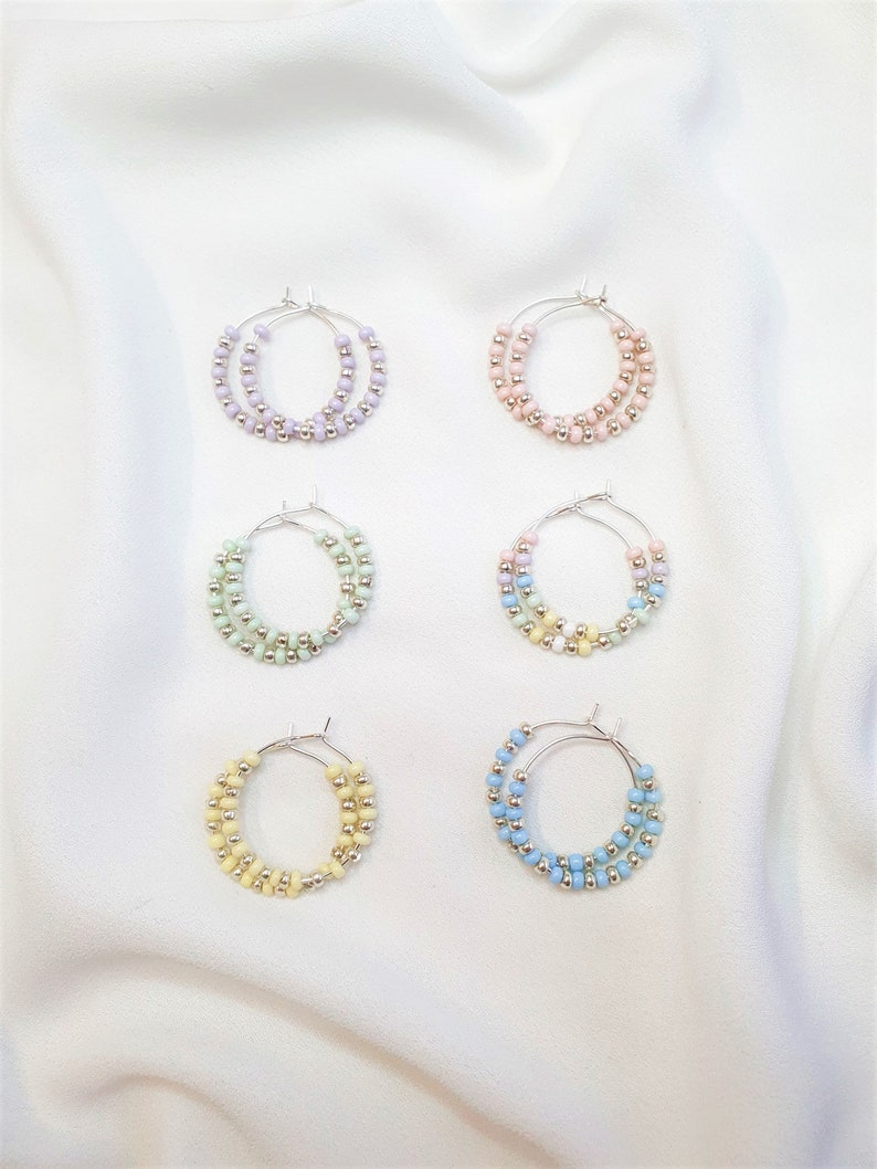 May include: Six pairs of hoop earrings with pastel colored beads. The earrings are arranged in two rows of three. The colors are lavender, pink, light green, light blue, yellow, and blue.