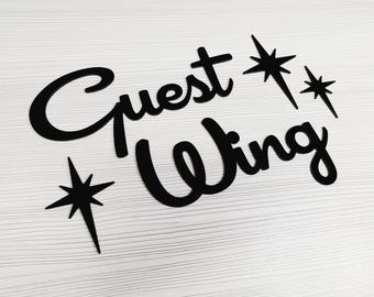 May include: Black cutout sign with the text "Guest Wing" in a retro font. The sign is decorated with three stylized stars.