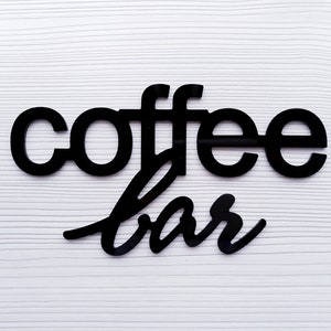 May include: Black wooden sign with the words "coffee bar" in a stylized font.