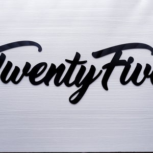 May include: Black cursive script lettering on a white background that reads "Twenty Five".