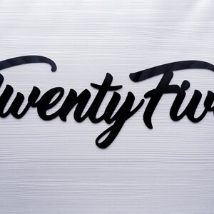 May include: Black cursive script letters spelling out "Twenty Five" on a white wood background.