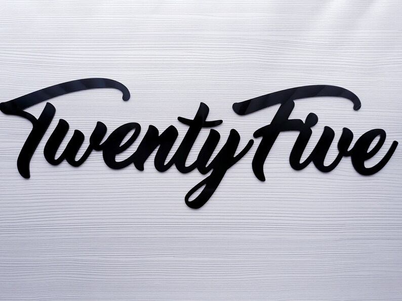 May include: Black cursive script letters spelling out "Twenty Five" on a white wood background.