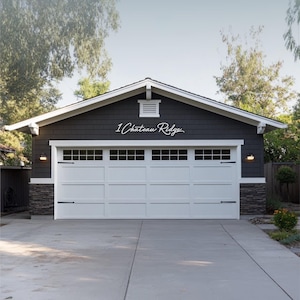 May include: A dark grey garage exterior featuring a white four-panel garage door with windows and black hardware. The text 1 Chateau Ridge is displayed in a white cursive script font on the dark grey siding above the garage door.
