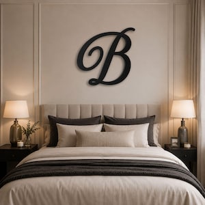 May include: A large, black, cursive letter B wall decoration mounted on a light-colored wall above a bed. The letter features a flowing, elegant script font with a smooth finish, centered horizontally to serve as a focal point in the room.