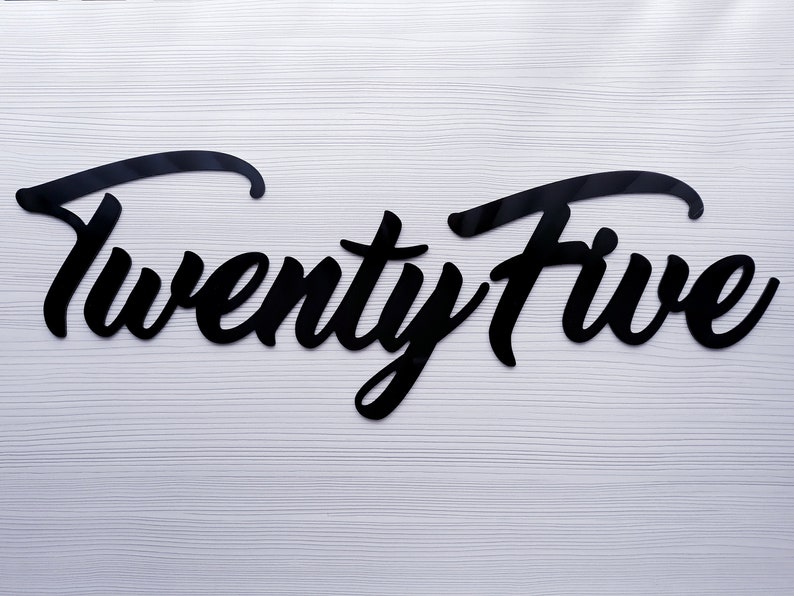 May include: Black acrylic cutout of the word "Twenty Five" in a cursive font.