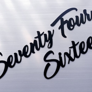 May include: Black cutout letters spelling out "Seventy Four Sixteen" on a white background.