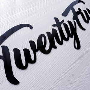 May include: Black acrylic cutout of the word "Twenty Five" in a cursive font.