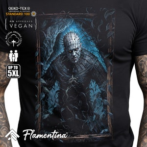 May include: Black t-shirt featuring a graphic print of a monster with spikes and a dark background. The monster is in a frame with vines growing around it. The text "Flamentina" is at the bottom of the shirt.