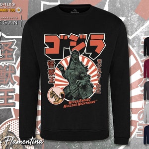 May include: Black long-sleeved sweatshirt featuring a graphic print of Godzilla, a Japanese monster, in front of a red sun. The text "ゴジラ" (Godzilla) is in Japanese characters above the monster. The text "怪獣王" (King of the Monsters) is to the left of the monster. The text "モンスターの王" (King of the Monsters) is to the right of the monster. The text "NEVER ENDING NUCLEAR NIGHTMARE" is below the monster.