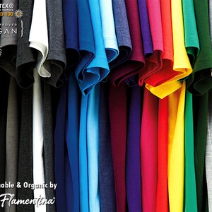 May include: A variety of t-shirts in different colors, hanging on a rack. The shirts are made of organic cotton and are certified vegan. The shirts are available in sizes up to 6XL. Oeko-Tex Standard 100, PITA Approved, Vegan, 100% Natural Organic Cotton, Up to 6XL, Sustainable & Organic by Flamentina.