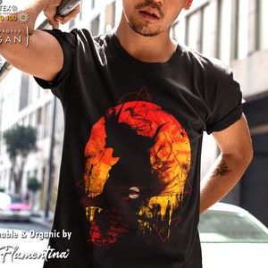 May include: Black t-shirt featuring a graphic print of a silhouette of a person in front of a red and orange sun with geometric shapes. The text "OEKO-TEX® STANDARD 100 TA-APPROVED VEGAN" is in the top left corner of the image. The text "Sustainable & Organic by Flamentina" is in the bottom left corner of the image.
