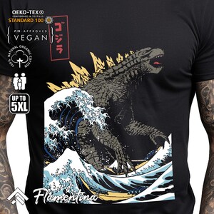 May include: Black t-shirt featuring a graphic print of Godzilla emerging from a large wave. The text "Gojira" is printed in Japanese characters on the shirt. The shirt also features the text "Flamentina" and the Oeko-Tex Standard 100 logo.