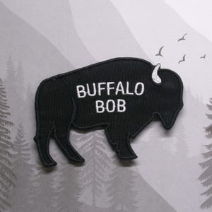 Puede incluir: Parche bordado negro con forma de b&uacute;falo con el texto "BUFFALO BOB" en blanco.