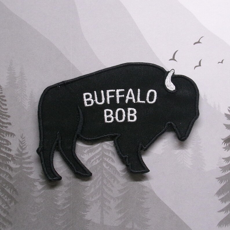Puede incluir: Parche bordado negro con forma de b&uacute;falo con el texto "BUFFALO BOB" en blanco.