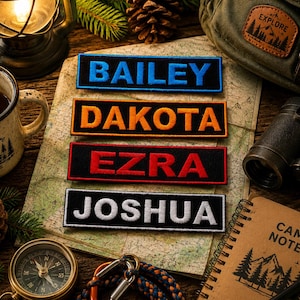 May include: Four embroidered name patches with the names BAILEY, DAKOTA, EZRA, and JOSHUA in bold letters. The patches are in blue, orange, red, and white, respectively, on black rectangular backgrounds. The patches are displayed on a map with camping gear.