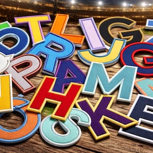 May include: A collection of colorful embroidered letters in various fonts and sizes, including yellow, orange, blue, and red, are arranged on a wooden surface. The letters are outlined in white and have a textured appearance, suggesting they are patches or appliques.